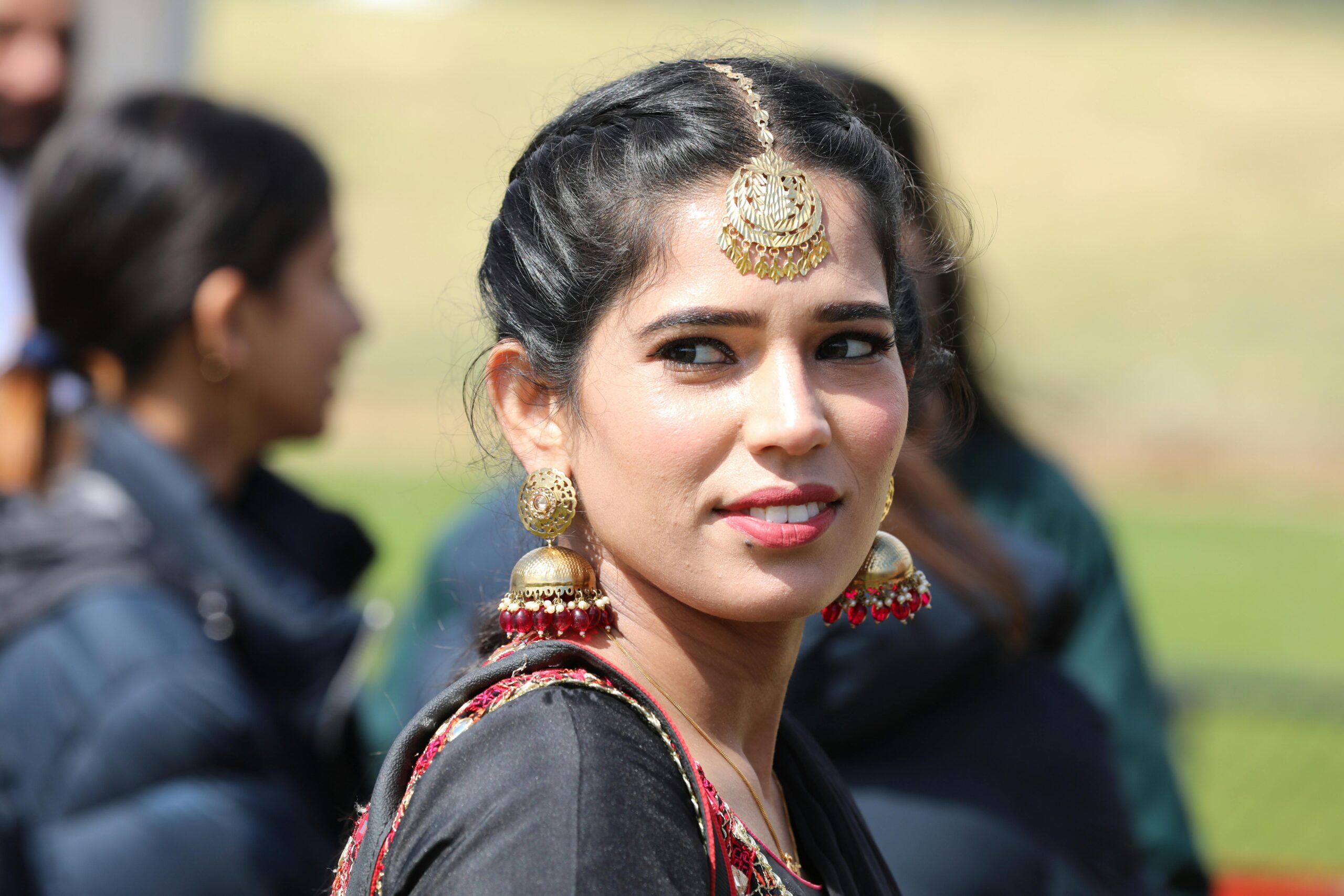 Portrait of a woman wearing ornate Indian jewelry, captured outdoors in a bright setting.